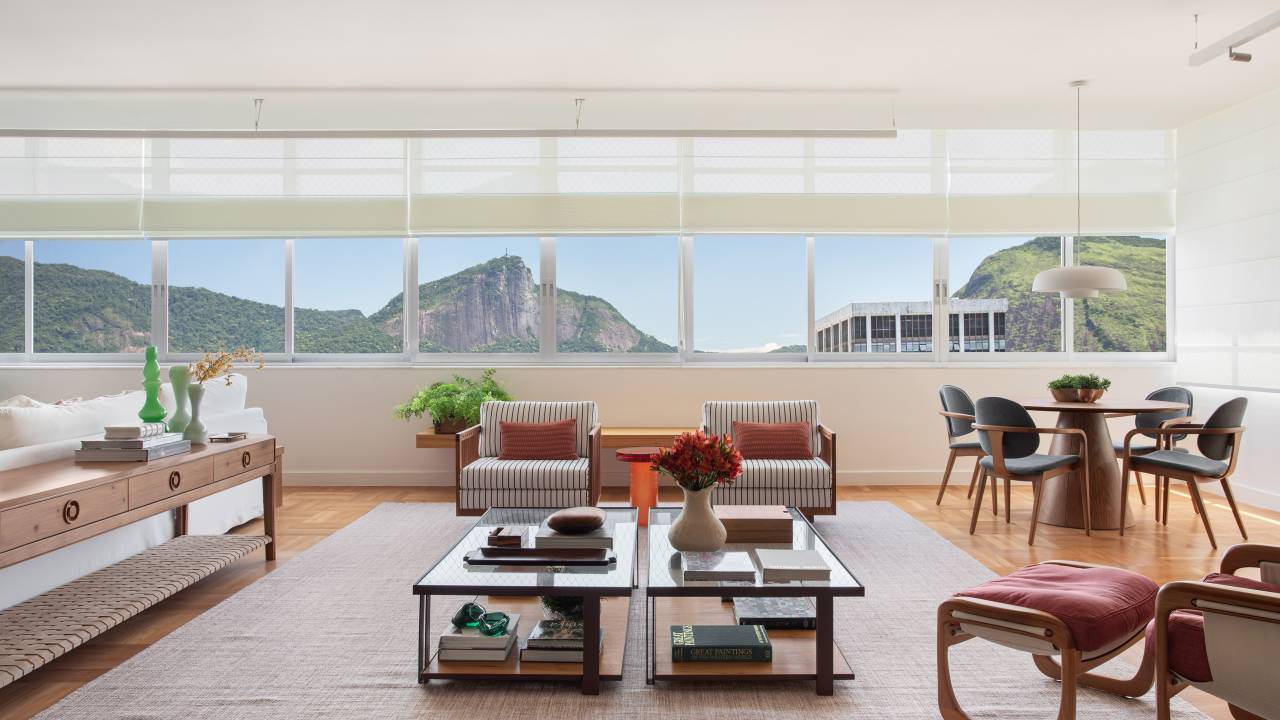 Reforma restaura piso de peroba e cria duas suítes em apê de 360 m². Projeto de Escala Arquitetura. Na foto, sala de estar com grandes janelas, tapete, mesa de centro com tampo de vidro.