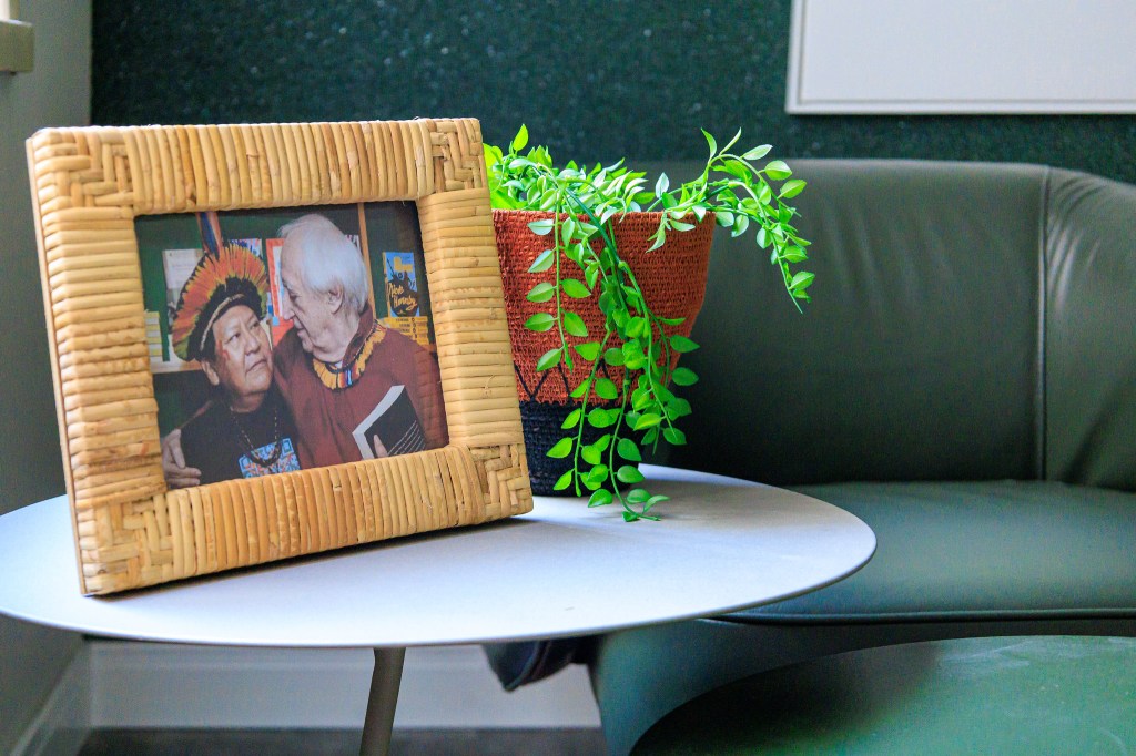 Sala é inspirada na obra de Zé Celso e na exuberância da Amazônia. Projeto de Jordana Fraga. Na foto, sala, mesa lateral com porta retrato, poltrona verde de couro, parede verde.
