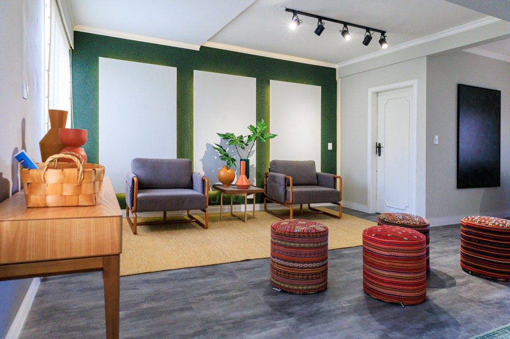 Sala é inspirada na obra de Zé Celso e na exuberância da Amazônia. Projeto de Jordana Fraga. Na foto, sala, duas poltronas, parede verde, trilho de spot.