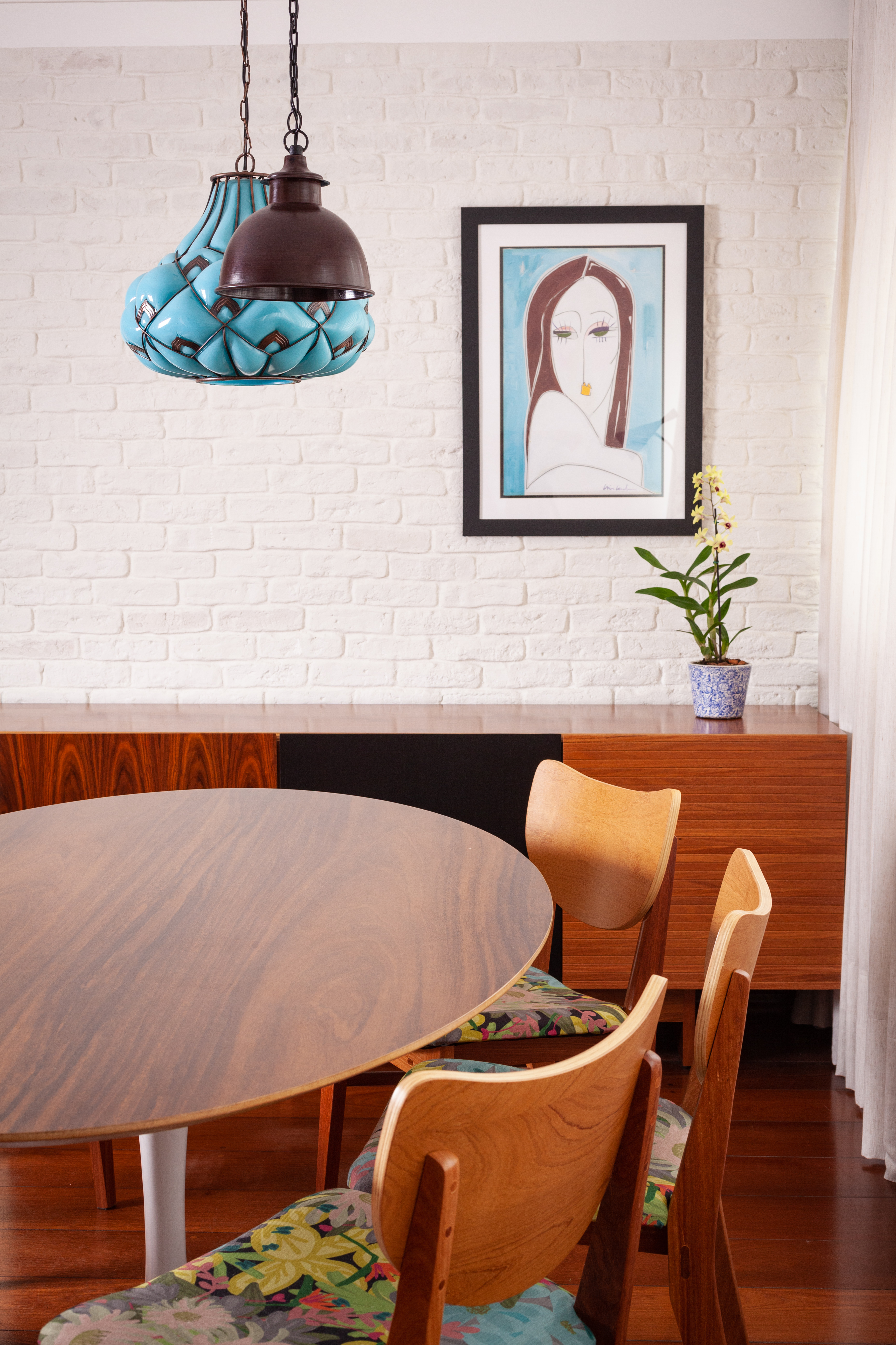Sem quebra-quebra, apê ganha nova atmosfera com móveis e texturas. Projeto de Abrazo Interiores. Na foto, sala de jantar, mesa redonda, buffet de madeira, luminária azul, parede de tijolinhos brancos.