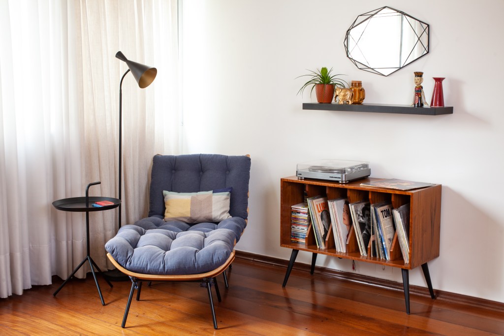 Sem quebra-quebra, apê ganha nova atmosfera com móveis e texturas. Projeto de Abrazo Interiores. Na foto, sala de estar, cantinho de leitura, poltrona costela azul, luminária de piso, rack com discos de vinil.