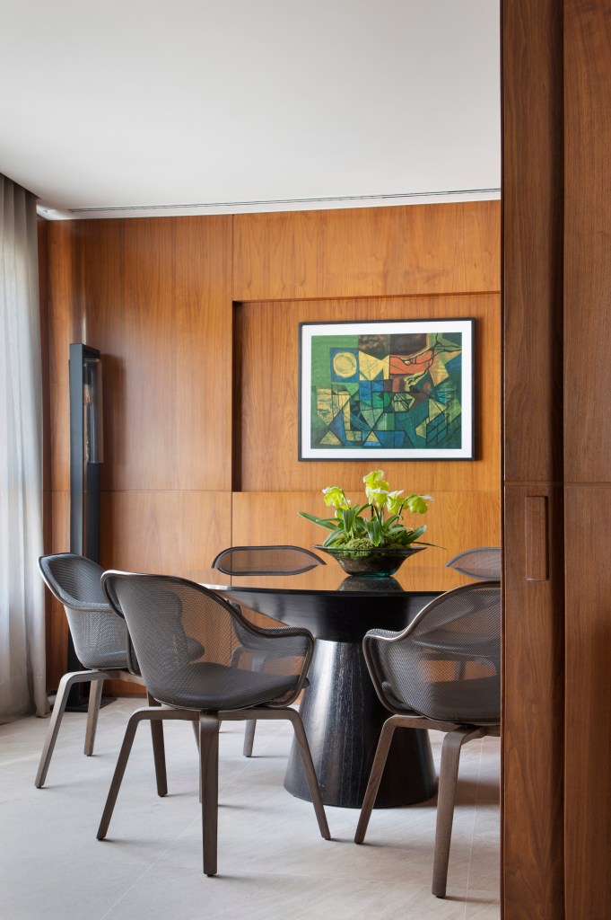 Tapete integra espaços da área social desta cobertura de 500 m². Projeto de DB Arquitetos. Na foto, copa de refeições com mesa redonda preta, parede com painel de madeira.