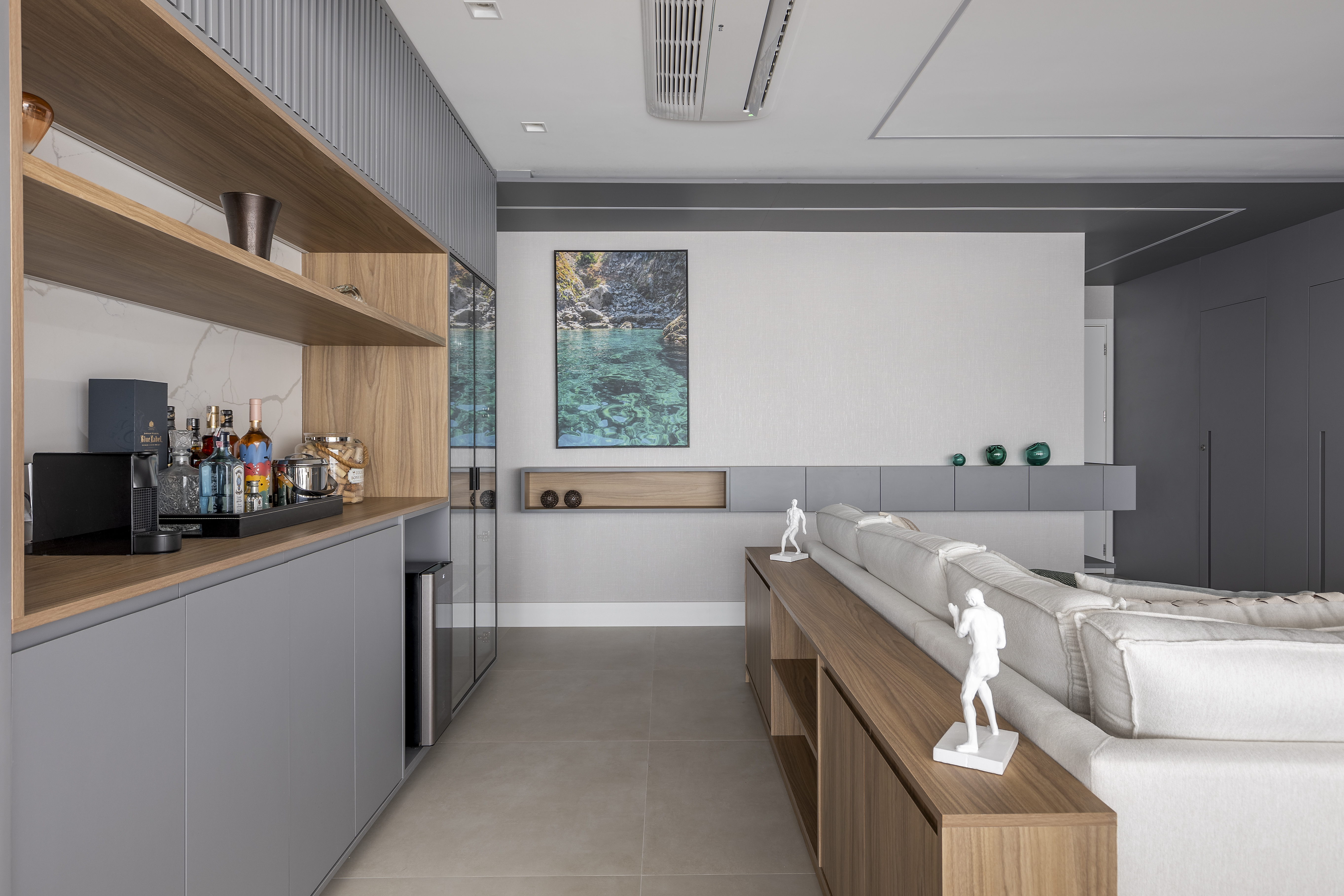 Varanda de apê tem dois espaços: um gourmet e outro de estar. Projeto de Blaia e Moura. Na foto, sala com aparador de madeira atrás do sofá.
