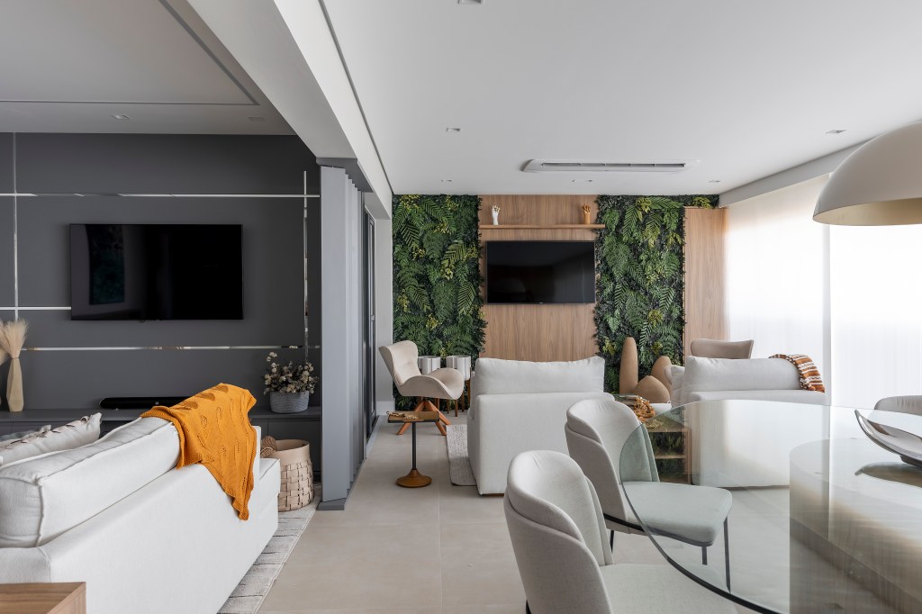 Varanda de apê tem dois espaços: um gourmet e outro de estar. Projeto de Blaia e Moura. Na foto, varanda com painel de tv, jardim vertical, sala de jantar.