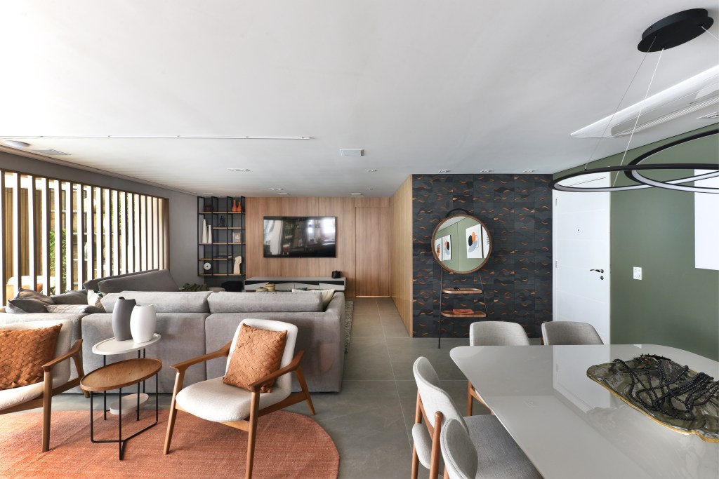 Varanda de estar gourmet é destaque em apartamento de 204 m². Projeto de Rosangela Pena. Na foto, sala de estar integrada, piso cinza, sofá cinza, poltronas brancas, tapete redondo em tom terroso.
