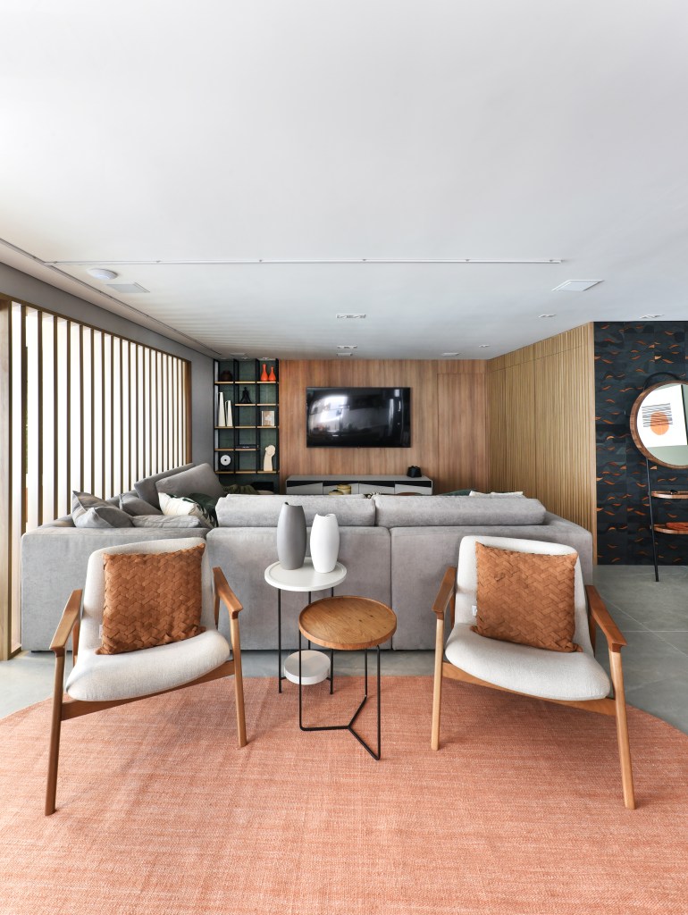 Varanda de estar gourmet é destaque em apartamento de 204 m². Projeto de Rosangela Pena. Na foto, sala de estar integrada, piso cinza, sofá cinza, poltronas brancas, tapete redondo em tom terroso.