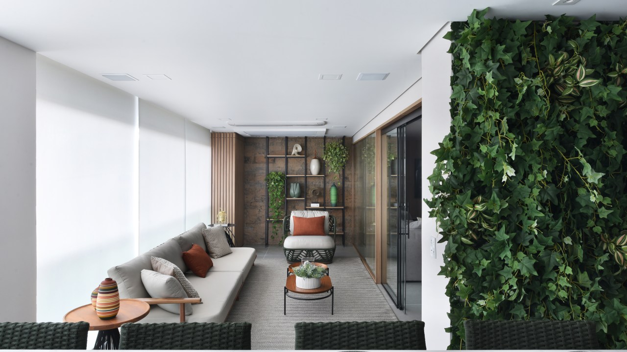 Varanda de estar gourmet é destaque em apartamento de 204 m². Projeto de Rosangela Pena. Na foto, cortina, sofá cinza, jardim vertical.