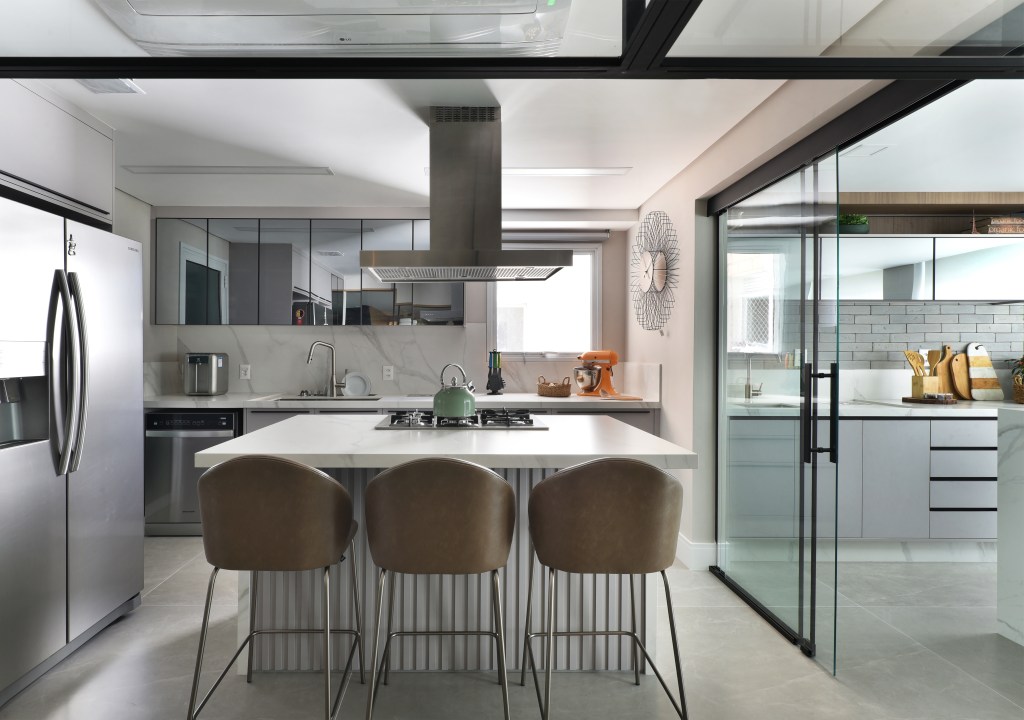 Varanda de estar gourmet é destaque em apartamento de 204 m². Projeto de Rosangela Pena. Na foto, cozinha com ilha e bancada marmorizada, banquetas, marcenaria cinza.