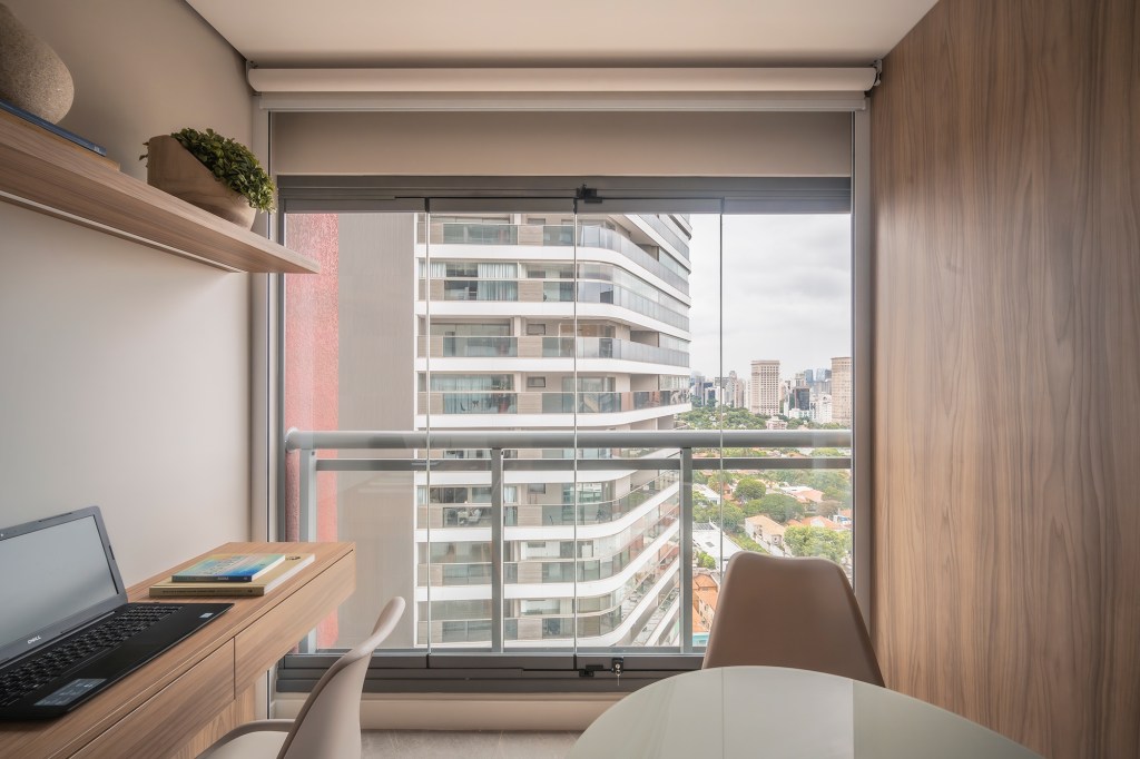 Varanda envidraçada otimiza a área de apartamento de apenas 24 m². Projeto de Gabriela Campanha. Na foto, home office na varanda fechada com vidro.