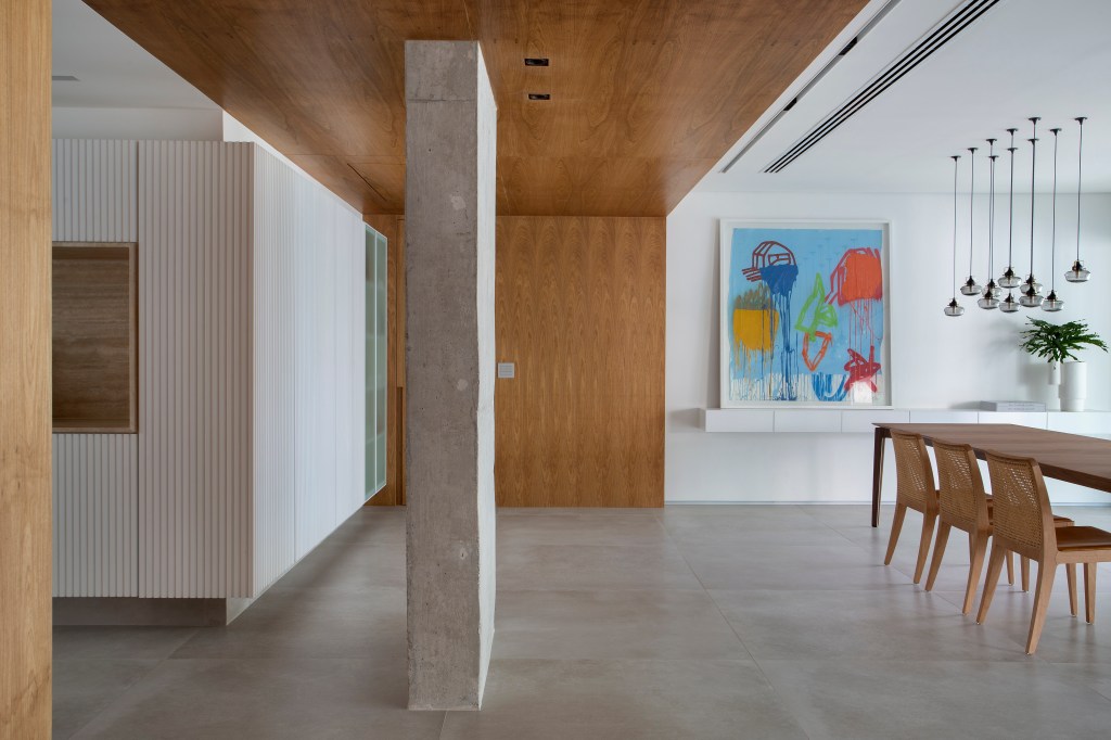 Venezianas em madeira trazem privacidade aos espaços de apê minimalista. Projeto de PKB Arquitetura. Na foto, hall, pilar de concreto, parede e teto revestidos com painel de madeira.