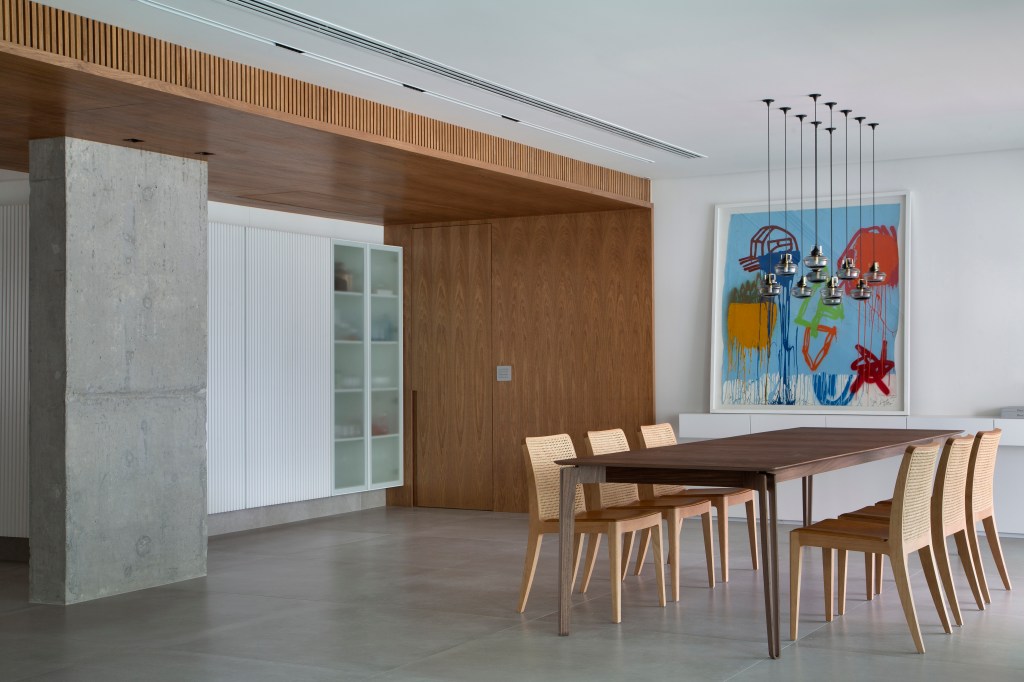 Venezianas em madeira trazem privacidade aos espaços de apê minimalista. Projeto de PKB Arquitetura. Na foto, sala integrada, piso de porcelanato, mesa de jantar, quadro.