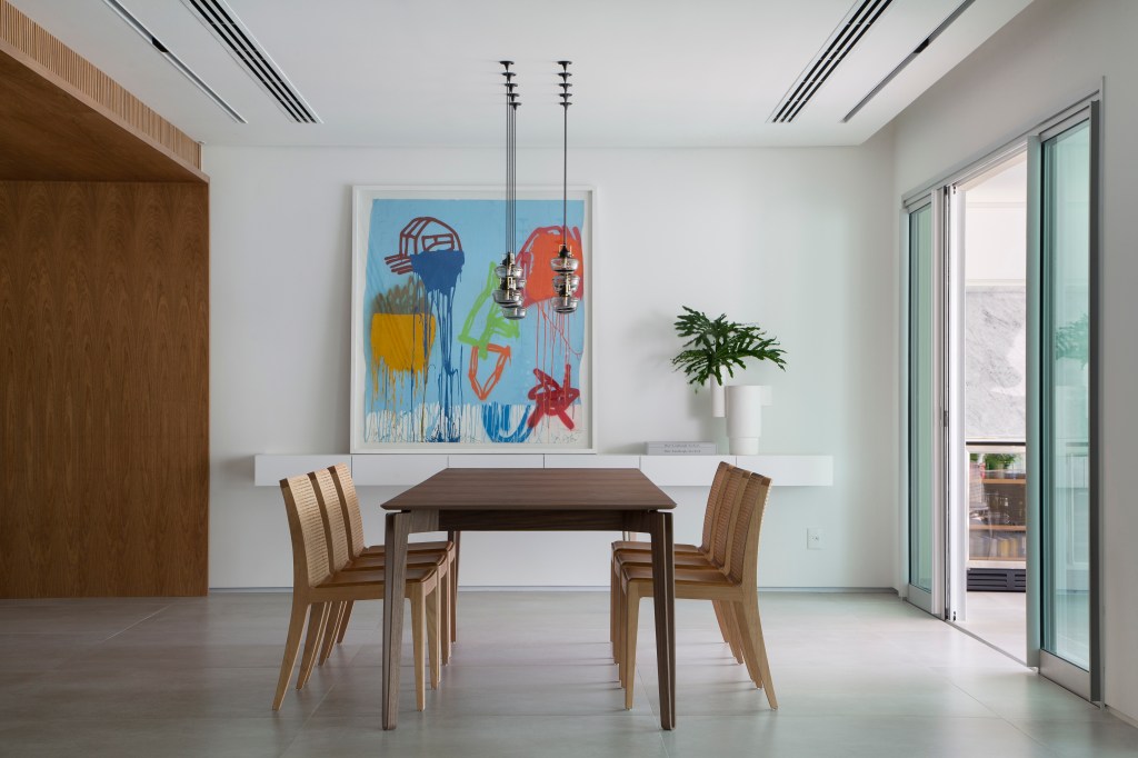 Venezianas em madeira trazem privacidade aos espaços de apê minimalista. Projeto de PKB Arquitetura. Na foto, sala de jantar, mesa, cadeiras, luminárias, quadro, aparador branco.