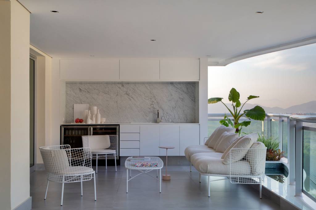 Venezianas em madeira trazem privacidade aos espaços de apê minimalista. Projeto de PKB Arquitetura. Na foto, sala minimalista branca, marcenaria branca com nicho marmorizado, piso de porcelanato.