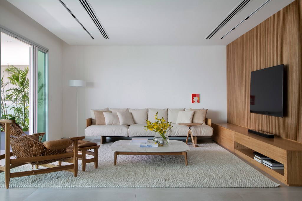 Venezianas em madeira trazem privacidade aos espaços de apê minimalista. Projeto de PKB Arquitetura. Na foto, sala de estar minimalista, sofá, mesa de centro com tampo branco.