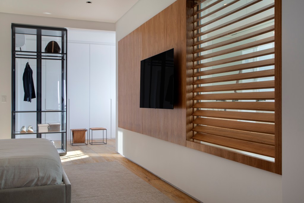 Venezianas em madeira trazem privacidade aos espaços de apê minimalista. Projeto de PKB Arquitetura. Na foto, painel de madeira, tv.