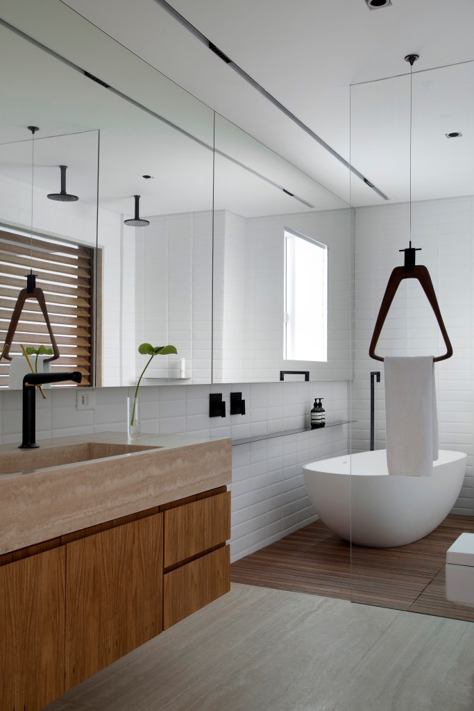 Venezianas em madeira trazem privacidade aos espaços de apê minimalista. Projeto de PKB Arquitetura. Na foto, banheiro, toalheiro suspenso, banheira solta.