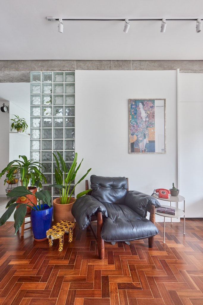 Vigas de concreto aparente emolduram área social de apê de 98 m². Projeto de Hugo Rapizo. Na foto, sala de estar, poltrona mole, parede de tijolos de vidro.