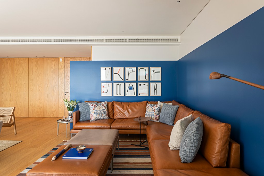Apartamento Estoril, em Portugal, ganha décor com brasilidade. Projeto de Andrea Chicharo. Na foto, sala de estar, sofá L de couro, parede azul, sofá listrado.