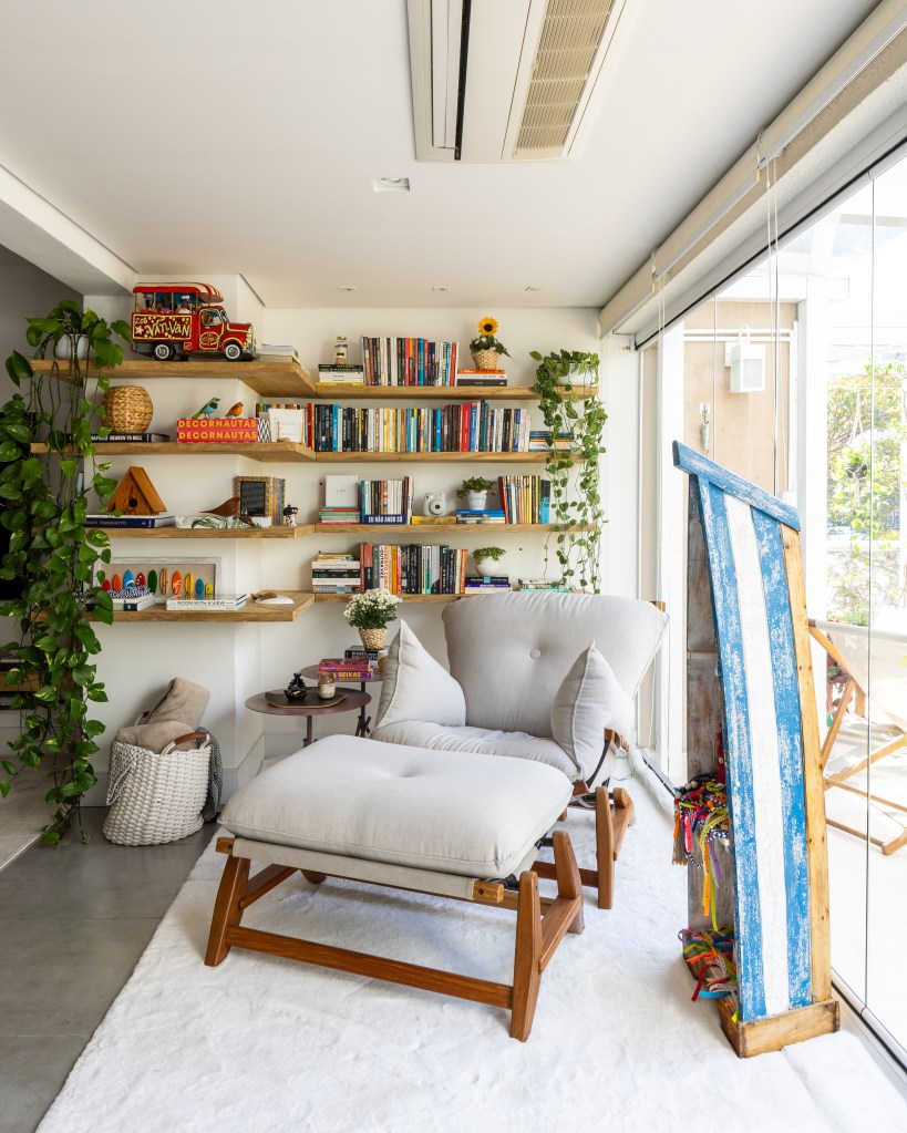 Apartamento em São Paulo tem decoração leve com livros e plantas. Projeto de Sou Arquitetura. Na foto, cantinho de leitura, poltrona com pufe, varanda, prateleira com livros, jiboia.