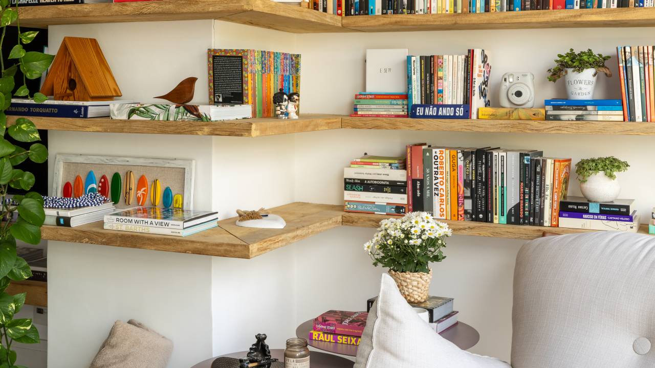 Apartamento em São Paulo tem decoração leve com livros e plantas. Projeto de Sou Arquitetura. Na foto, cantinho de leitura, poltrona com pufe, varanda, prateleira com livros, jiboia.