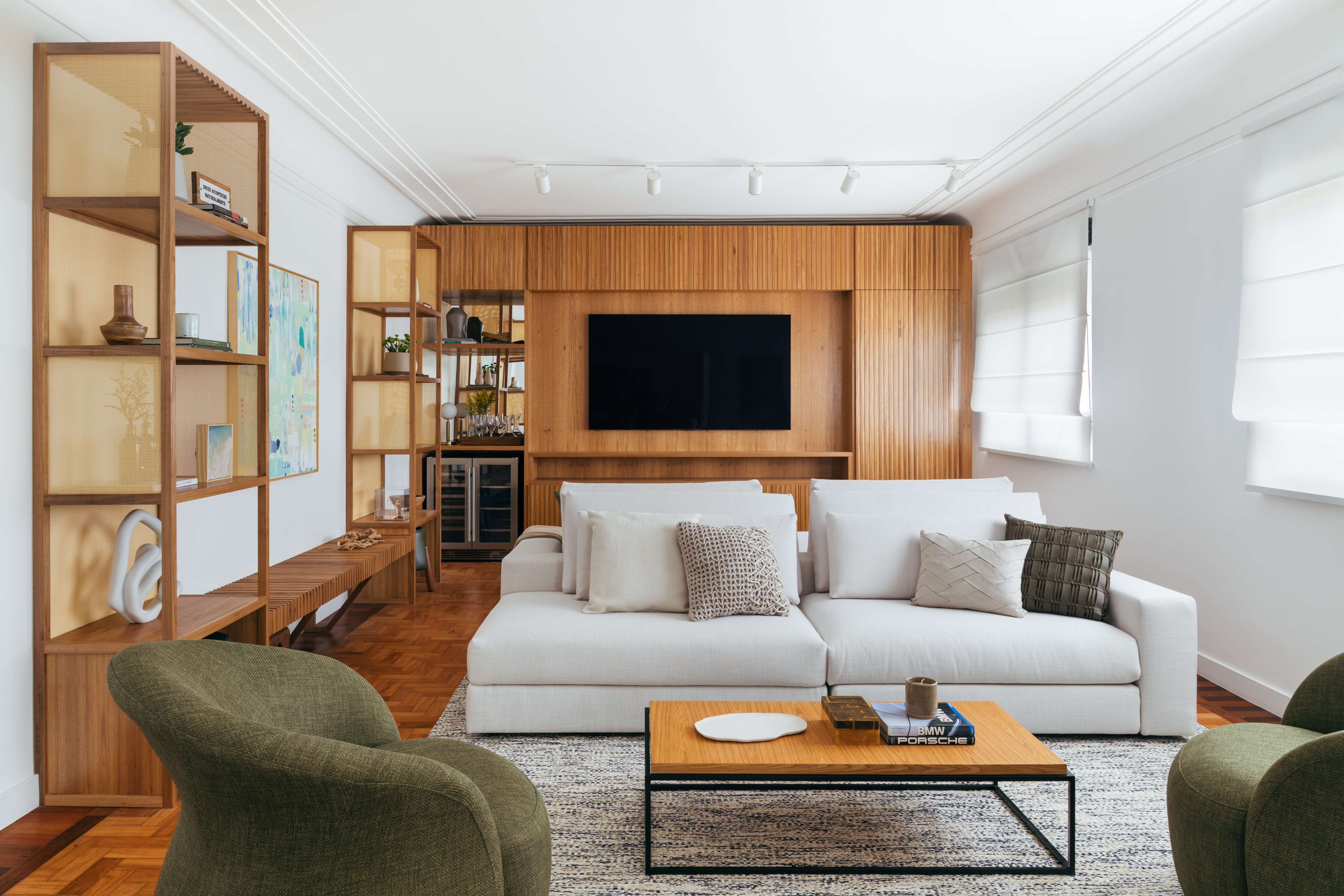 Apê de 200 m² tem varanda com banco verde e hall de orações. Projeto de Fernanda Medeiros. Na foto, sala de estar, sofá branco, poltrona verde musgo, painel de madeira, tv.