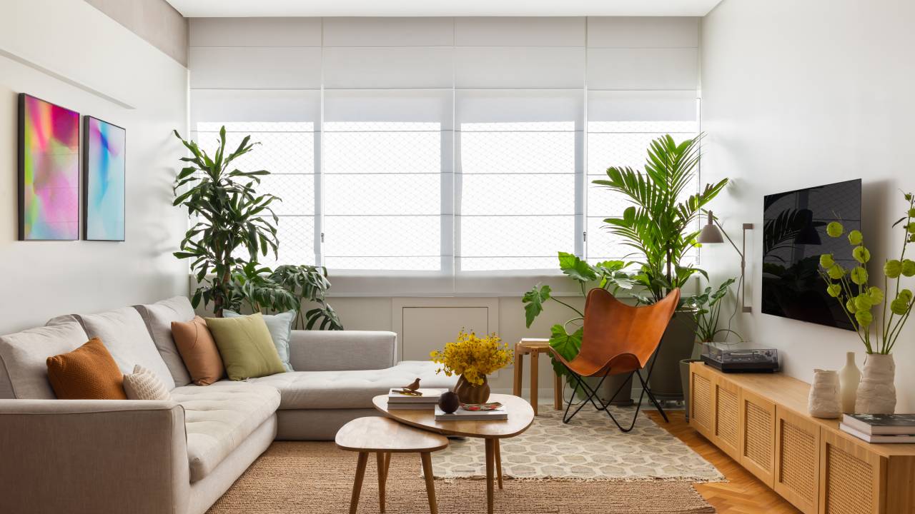 Apê ganha escritório com vista para o mar e texturas nas paredes brancas. Projeto Ateliê Concreto. Na foto, sala com tapete, poltrona, tv e aparador com porta de tela.