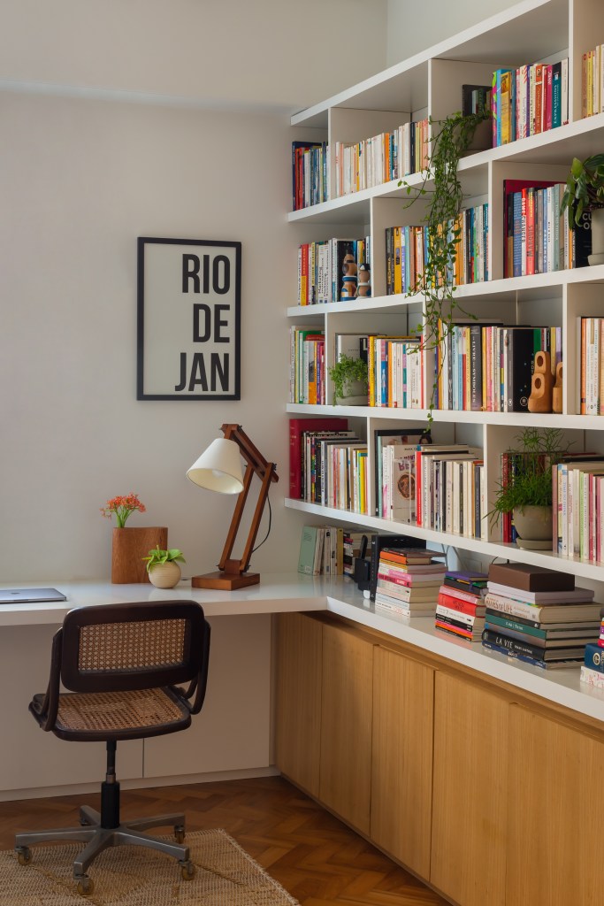 Apê ganha escritório com vista para o mar e texturas nas paredes brancas. Projeto Ateliê Concreto. Na foto, home office com prateleiras de livros.