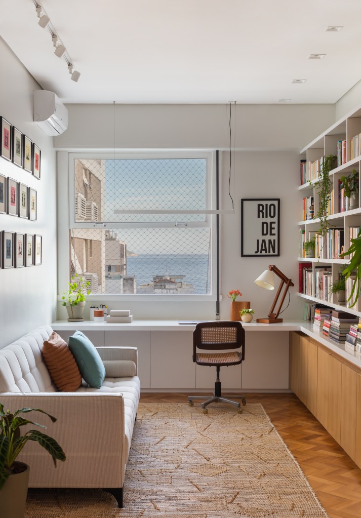 Apê ganha escritório com vista para o mar e texturas nas paredes brancas. Projeto Ateliê Concreto. Na foto, home office com prateleiras de livros.