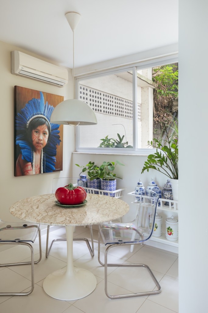 Apê ganha copa de cozinha e suíte voltada para pequeno jardim interno. Projeto de Vivian Reimers. Na foto, mesa redonda pequena, cadeiras transparente, luminária, ar condicionado.