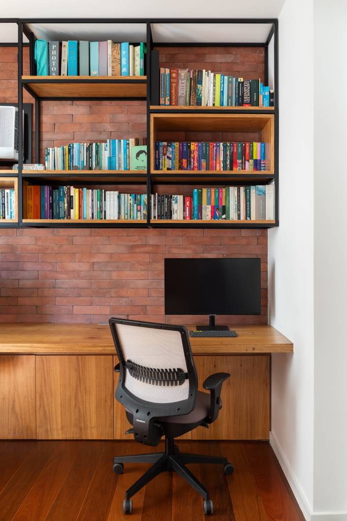 Apê ganha estante para livros e discos de vinil e paredes com ladrilhos. Projeto de Co+Lab Juntos Arquitetura. Na foto, home office, parede de tijolinhos terracota, bancada de madeira, prateleira suspensa.