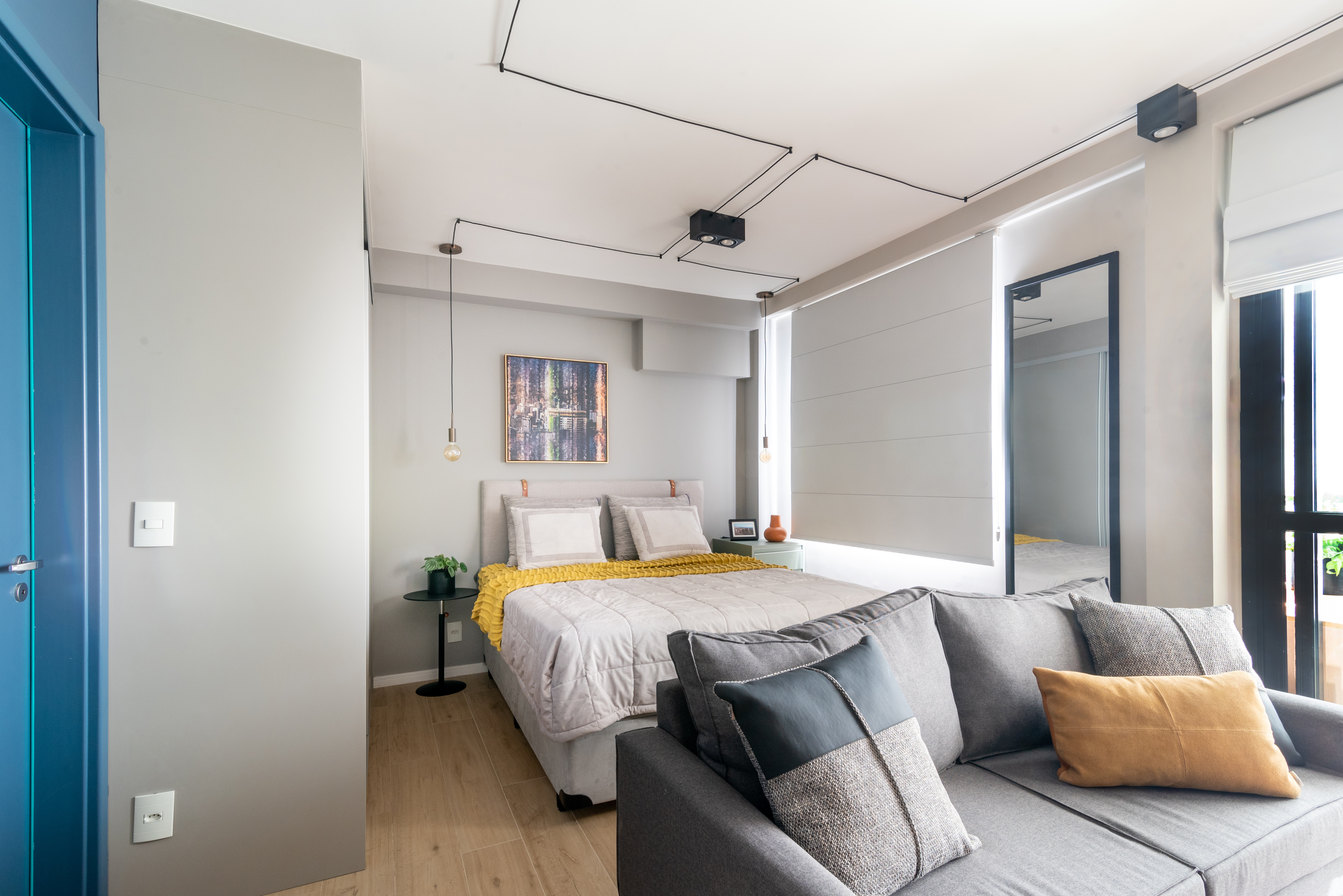 Caixa de marcenaria verde abriga cozinha, bancada e tv em estúdio de 34 m². Projeto de Abrazo Arquitetura. Na foto, quarto com cama de casal, sofá cinza.