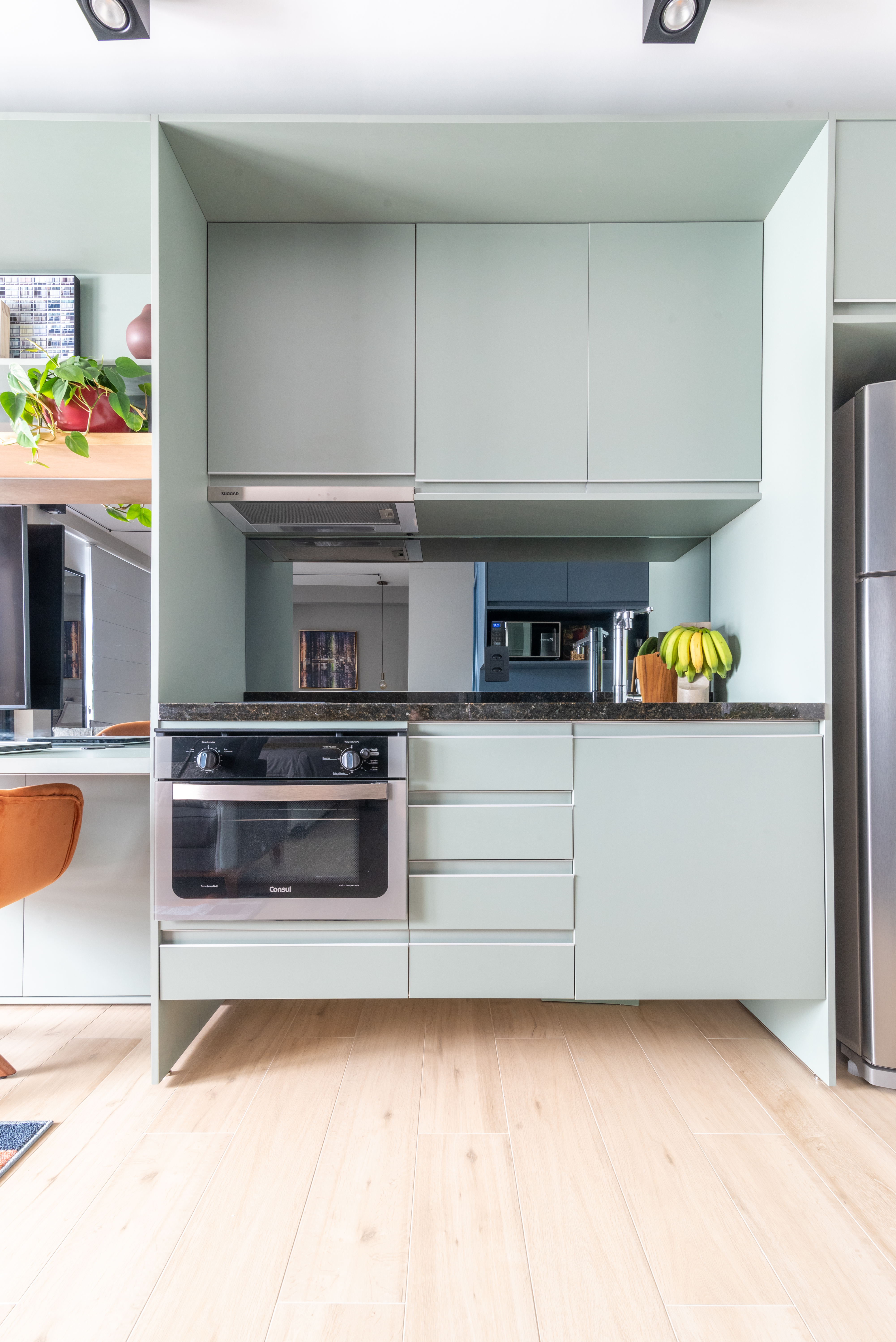 Caixa de marcenaria verde abriga cozinha, bancada e tv em estúdio de 34 m². Projeto de Abrazo Arquitetura. Na foto, cozinha pequena com marcenaria verde clara.
