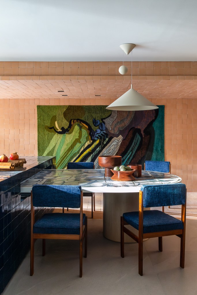 Cerâmicas artesanais compõem o tampo da mesa desta cozinha repleta de azul. Projeto de Mandril Arquitetura. Na foto, cozinha com bancada azul, mesa de azulejos e tijolinhos.