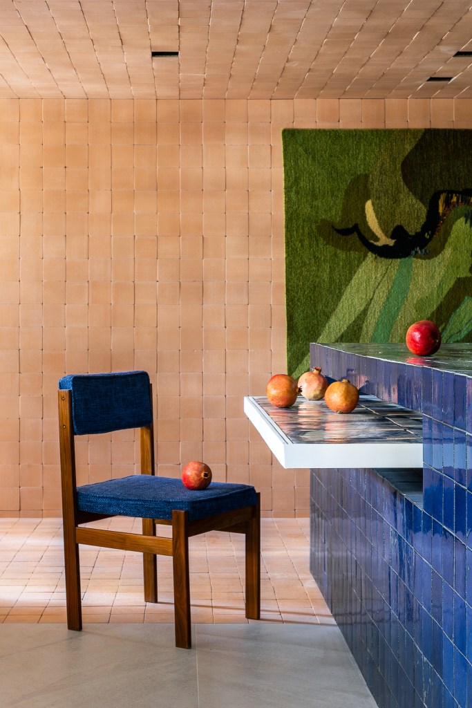 Cerâmicas artesanais compõem o tampo da mesa desta cozinha repleta de azul. Projeto de Mandril Arquitetura. Na foto, cozinha com bancada azul, mesa de azulejos e tijolinhos.