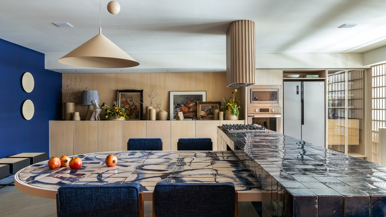 Cerâmicas artesanais compõem o tampo da mesa desta cozinha repleta de azul. Projeto de Mandril Arquitetura. Na foto, cozinha com bancada azul e mesa estampada de cerâmica.