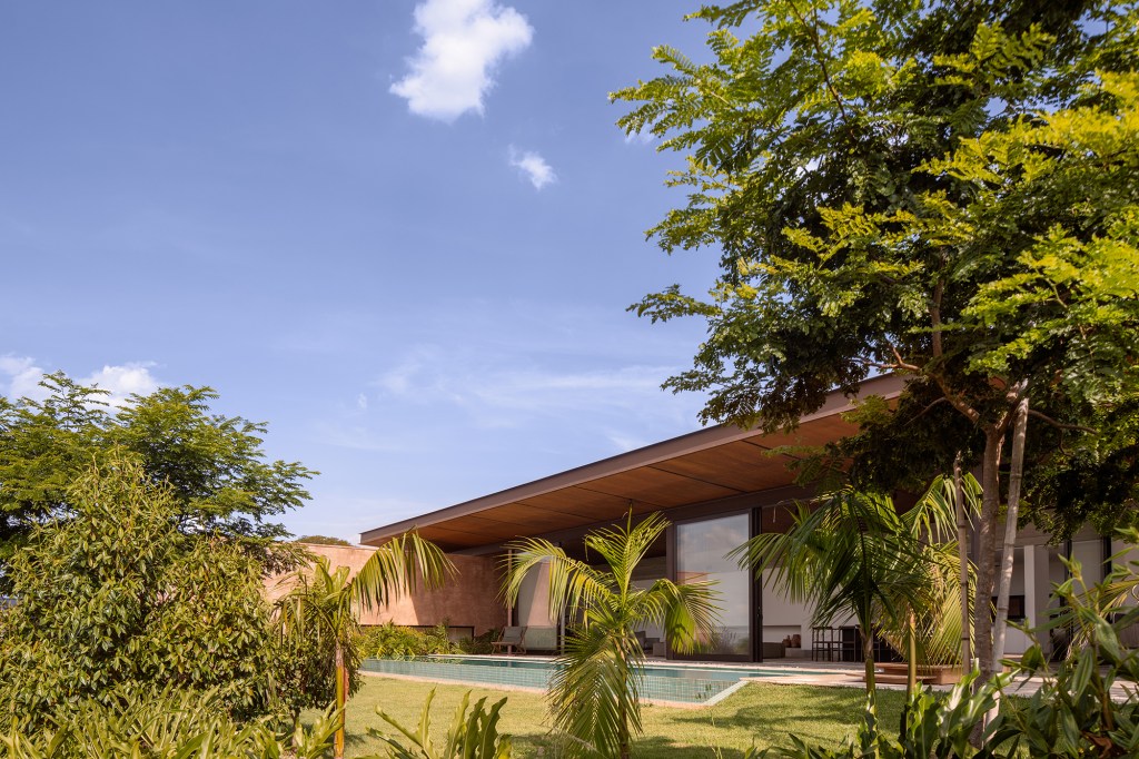 Cobertura metálica unifica os volumes desta casa de 568 m². Projeto de Vaga Arquitetura. Na foto, fachada com piscina e jardim.