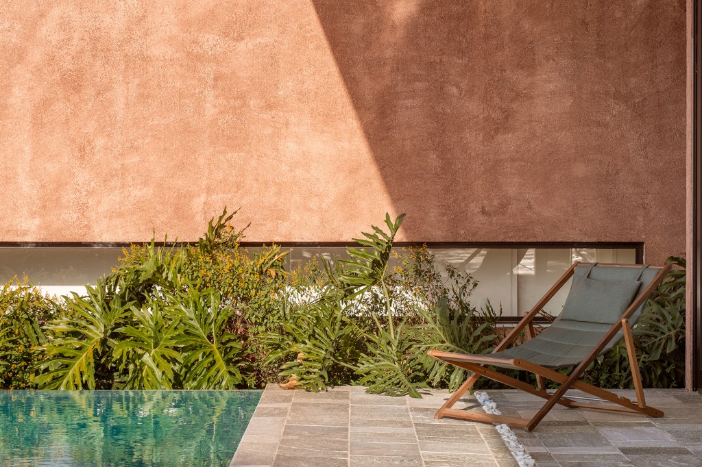Cobertura metálica unifica os volumes desta casa de 568 m². Projeto de Vaga Arquitetura. Na foto, jardim com varanda, piscina e plantas.