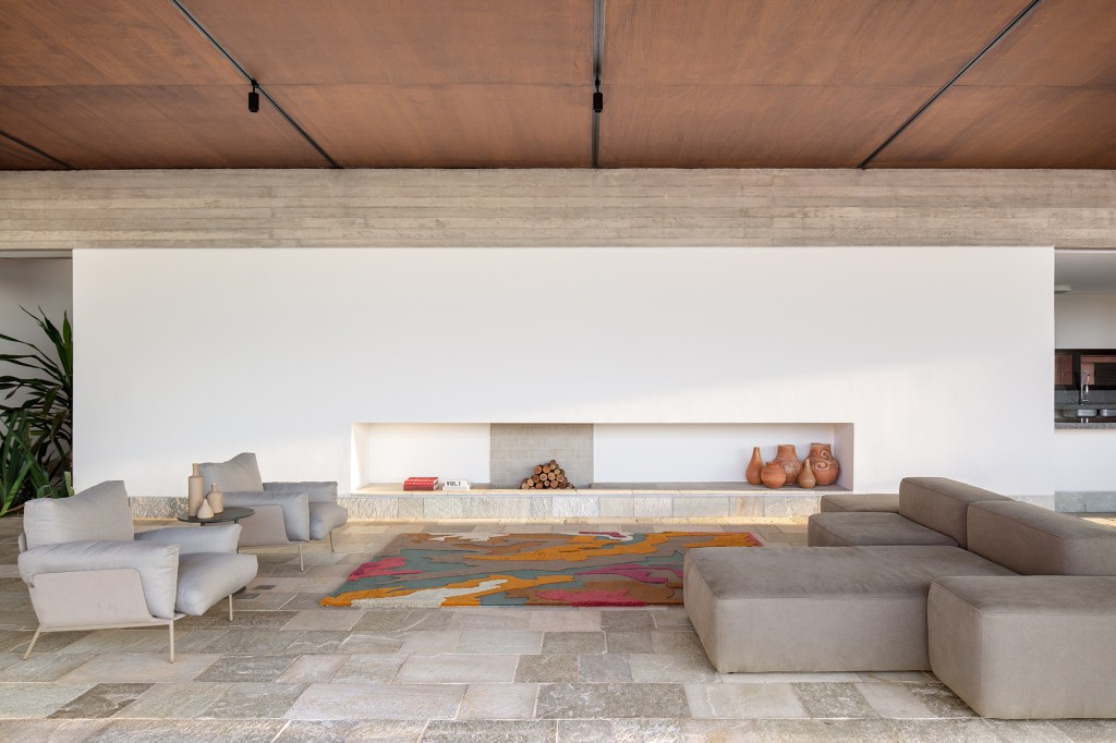 Cobertura metálica unifica os volumes desta casa de 568 m². Projeto de Vaga Arquitetura. Na foto, sala com lareira, sofá e piso de pedra.