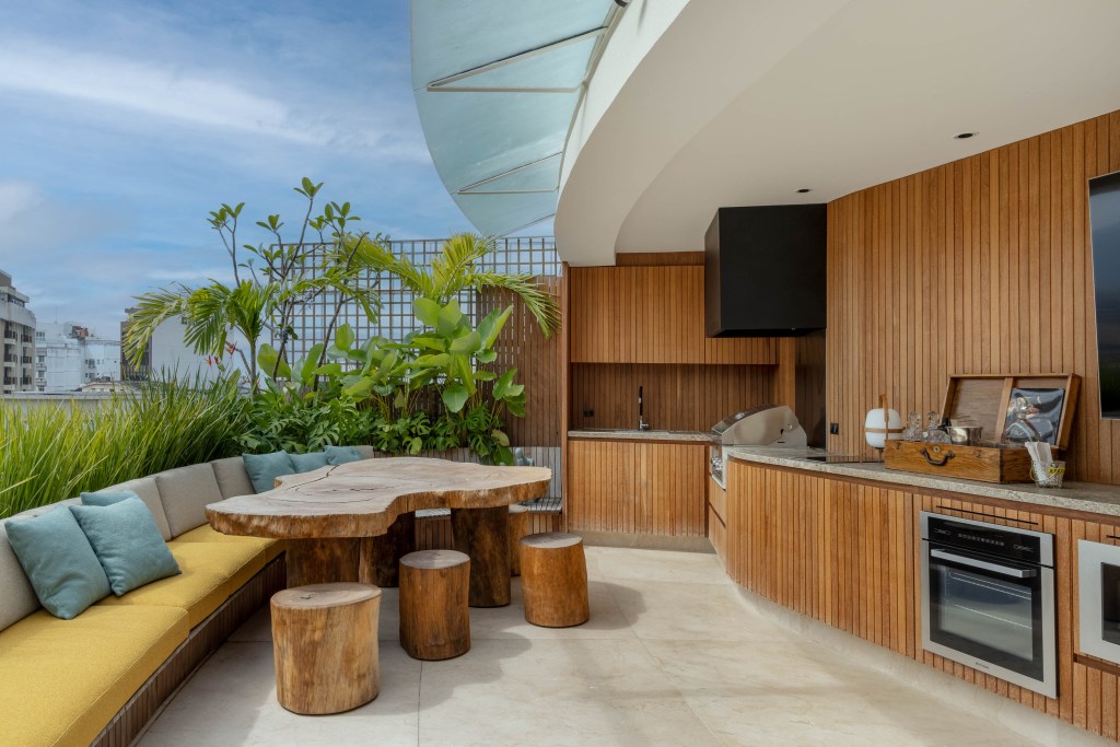 Cobertura com planta circular tem jardim interno, área gourmet e sauna. Projeto de Roberto Souto. Na foto, mesa rústica de madeira, plantas.