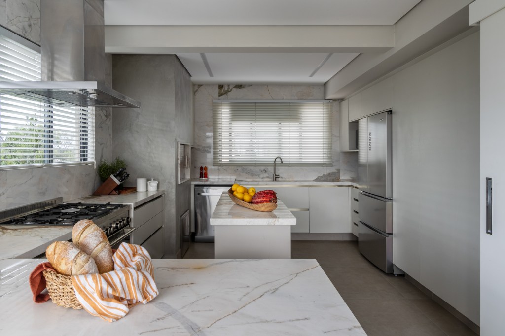 Cozinha integrada ao jardim é o coração deste apartamento de 282 m². Projeto Estudio Elmor. Na foto, cozinha com ilha, parede de cimento e marcenaria,