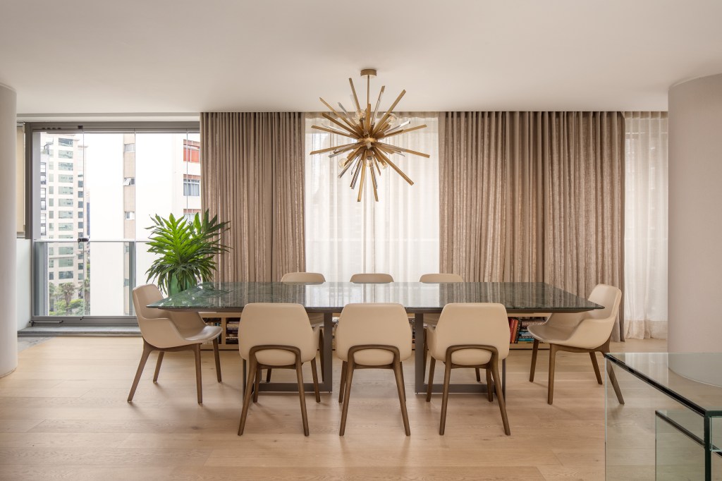 Cozinha revestida com quartzito é destaque no apê da chef Carol Magalhães. Projeto de DB Arquitetos. Na foto, sala de jantar, lustre, mesa com tampo de pedra, cortina.