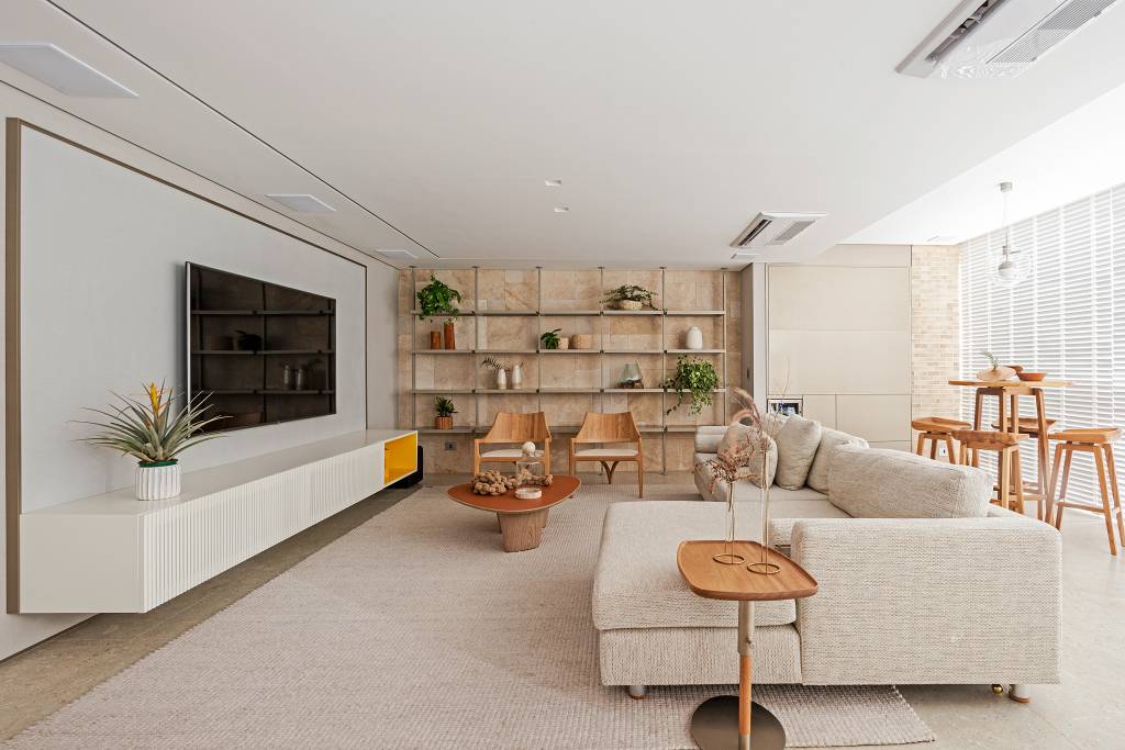 Décor que remete à praia pauta o apê de 140 m² do morador amante do surfe. Projeto do Estúdio Elmor. Na foto, sala com sofá, poltrona suspensa e estante.