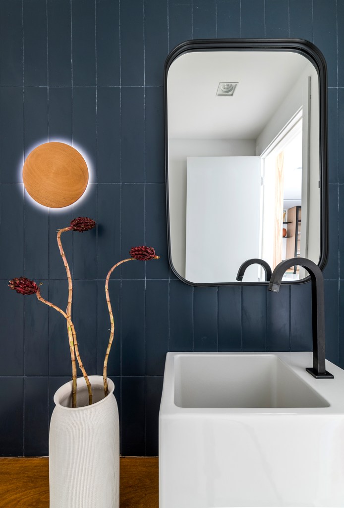 Dois escritórios e ampla área de receber caracterizam apê de 175 m². Projeto de Juliana Casadei. Na foto, lavabo com arandela, espelho e revestimento azul.