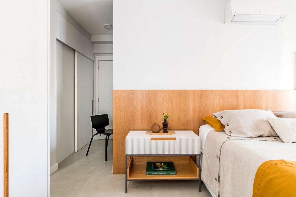Dois escritórios e ampla área de receber caracterizam apê de 175 m². Projeto de Juliana Casadei. Na foto, quarto de casal com cabeceira de madeira, quadro e mesinhas.