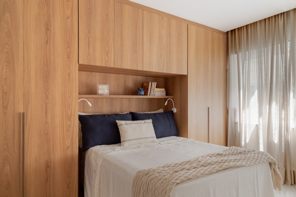 Espelho oval e armário em volta da cama são destaques em apê de 67 m². Projeto de Mariana Monnerat. Na foto, quarto, almofada azul, prateleira, manta.