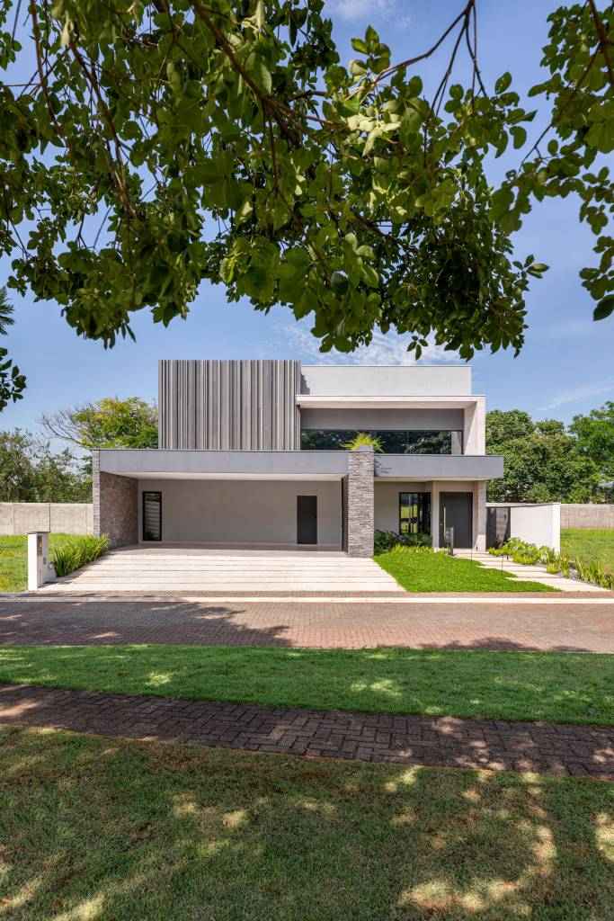 Filetes em madeira ecológica revestem entrada de casa de 350 m². Projeto de Augusto Manzato Arquitetura. Na foto, fachada, gramado.