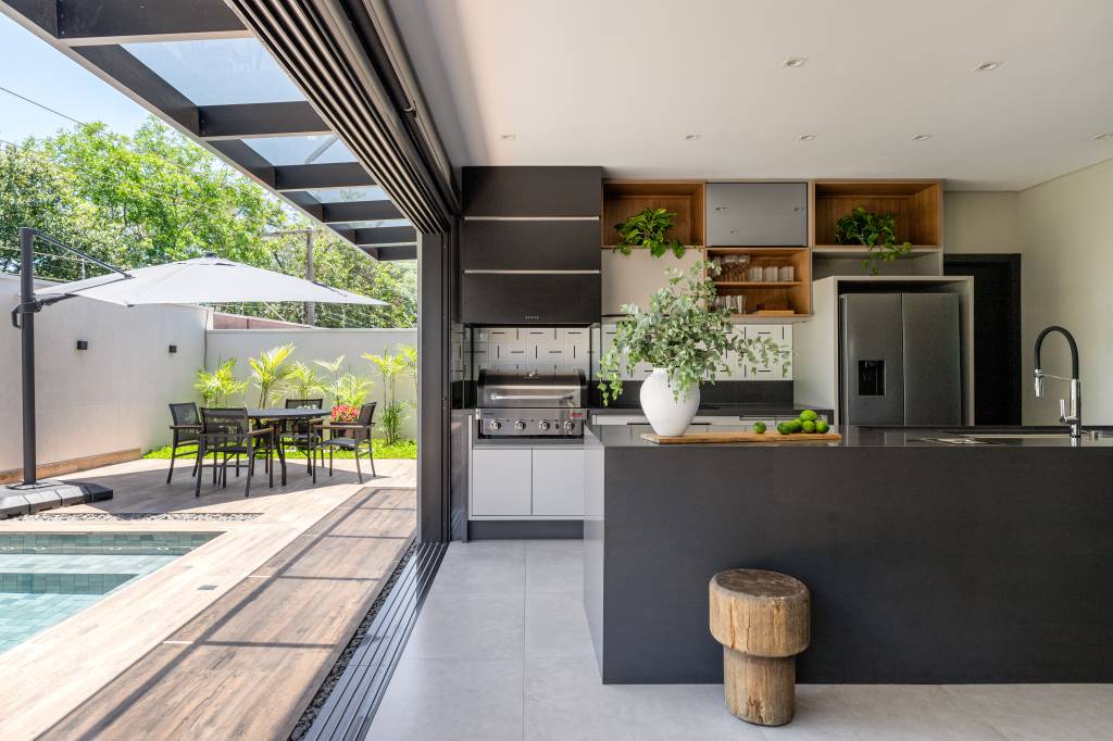 Filetes em madeira ecológica revestem entrada de casa de 350 m². Projeto de Augusto Manzato Arquitetura. Na foto, área gourmet, churrasqueira, bancada preta.