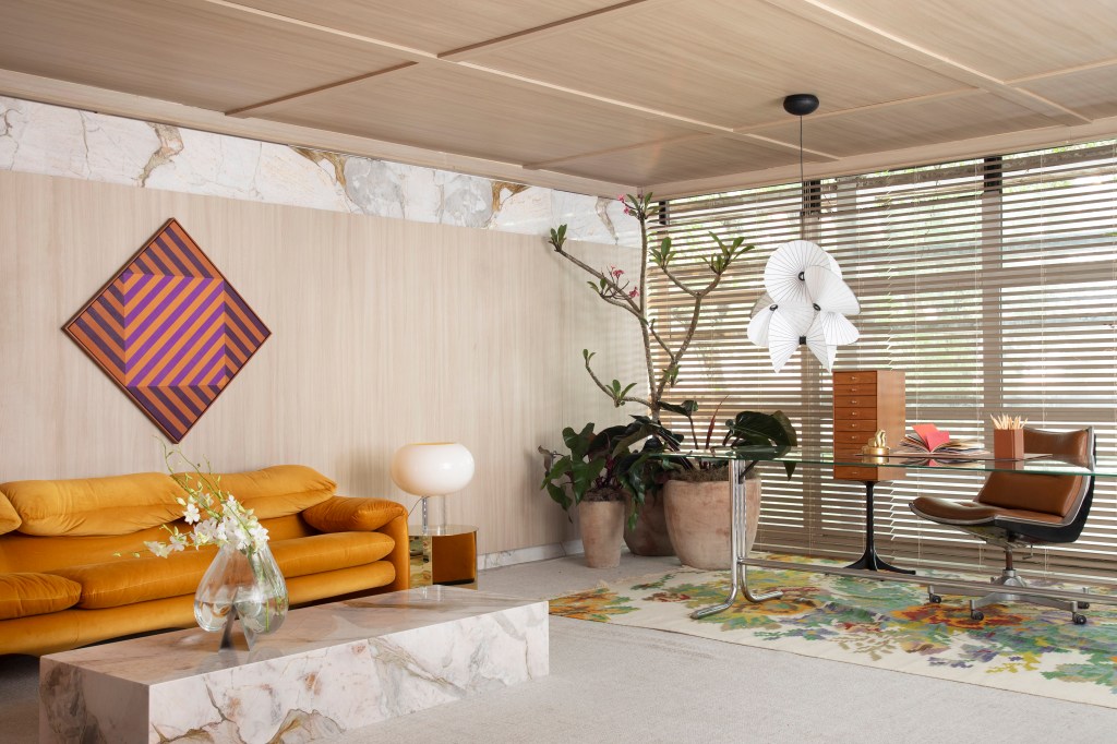 Home office de 45 m² tem estante de marcenaria e mármore e área de estar. Projeto de Rodolfo Consoli para a CASACOR São Paulo 2024. Na foto, planta, sofá terracota, luminária.