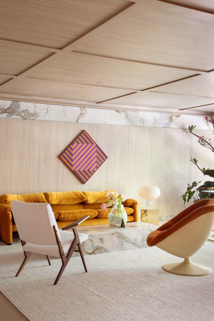 Home office de 45 m² tem estante de marcenaria e mármore e área de estar. Projeto de Rodolfo Consoli para a CASACOR São Paulo 2024. Na foto, sofá terracota, painel de madeira, mesa de centro.