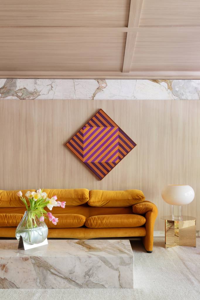 Home office de 45 m² tem estante de marcenaria e mármore e área de estar. Projeto de Rodolfo Consoli para a CASACOR São Paulo 2024. Na foto, sofá terracota, painel de madeira, mesa de centro.